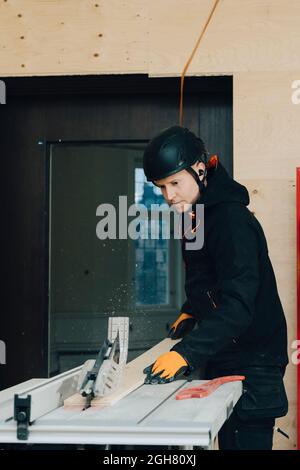 Male worker using table saw for cutting wooden plank while working at construction site Stock Photo