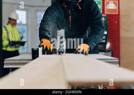 Midsection of male worker using table saw for cutting wooden plank at construction site Stock Photo