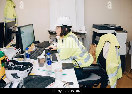 Side view of female engineer sitting with hand on chin while working on computer in office Stock Photo
