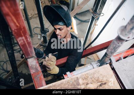 Young male welder wearing welding helmet while working at construction site Stock Photo