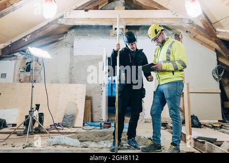 Full length of male construction workers discussing over digital tablet while working at site Stock Photo