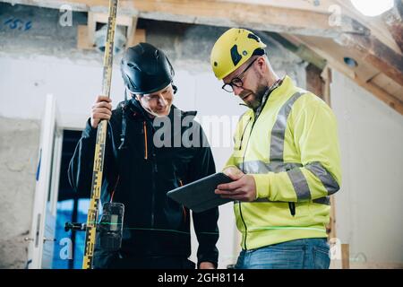 Male construction workers discussing over digital tablet while working at site Stock Photo