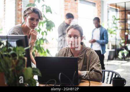 Female computer programmers discussing over laptop while Stock Photo