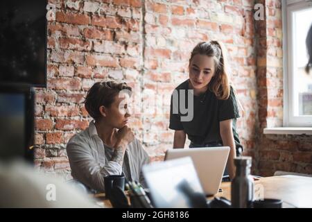 Businesswoman discussing with female colleague over laptop at office Stock Photo