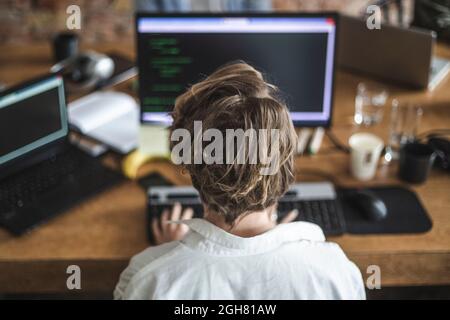 Rear view of female programmer coding on computer in office Stock Photo