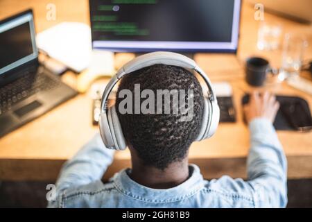 Rear view of male hacker working on computer at office Stock Photo