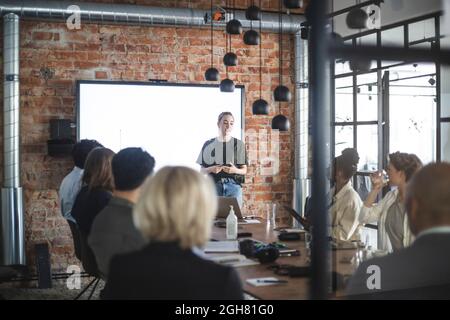 Young businesswoman giving presentation to colleagues during meeting at office Stock Photo
