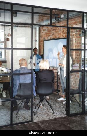 Female computer programmer giving presentation to advisors seen through doorway of startup company Stock Photo