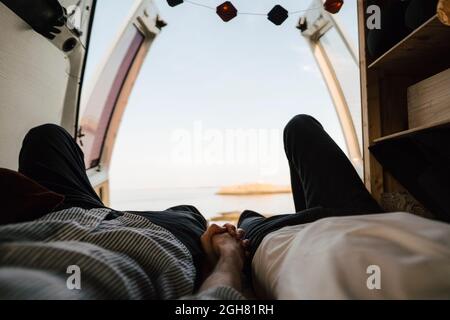 Midsection of gay couple holding hands while resting in camping van at lakeshore Stock Photo