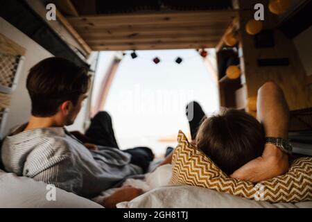 Male friends lying down on bed in camping van Stock Photo