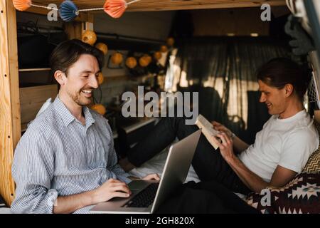 Smiling man using laptop sitting by boyfriend in camping van Stock Photo
