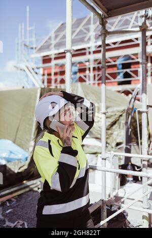 Female builder talking on mobile phone standing at scaffolding Stock Photo