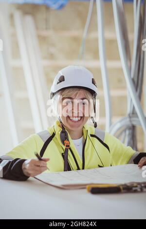 Portrait of happy female building contractor with floor plan at construction site Stock Photo