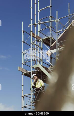 Female builder talking on mobile phone while standing at scaffolding Stock Photo