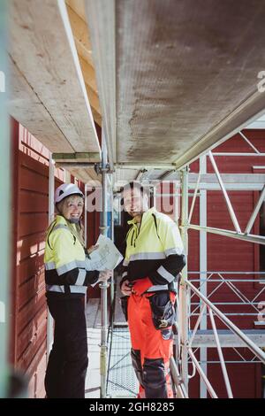 Smiling female builder with male colleague discussing while standing together at scaffolding Stock Photo