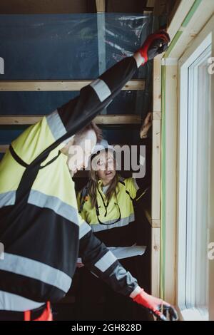 Female builder looking at male colleague measuring window frame at construction site Stock Photo