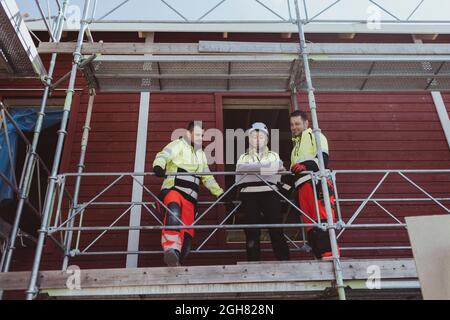 Female building contractor discussing over floor plan with male colleagues at scaffolding Stock Photo