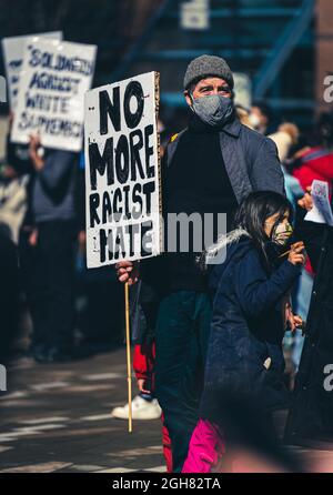 VANCOUVER, CANADA - Apr 12, 2021: A man in a mask with a young daughter holding a sign of no more racist hate in Vancouver, Canada Stock Photo