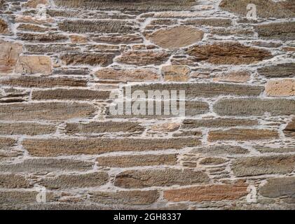 Ancient natural brown stone wall with gray cement background. Irregular masonry Stock Photo