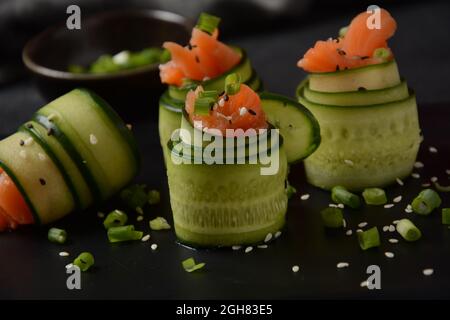 Cucumber rolls with pieces of salted salmon, black and white sesame seeds, chopped green onion. Holiday vegetable appetizers Stock Photo
