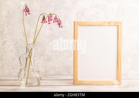 Wooden frame with pink dicentra, broken heart in glass on gray concrete background. side view, copy space, mockup, template, spring, summer minimalism Stock Photo