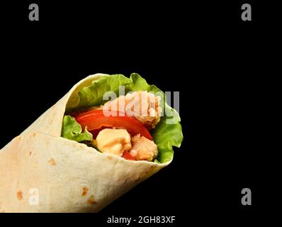 Classic tortilla wrap roll with grilled chicken and vegetables, tomato, lettuce on black  Stock Photo