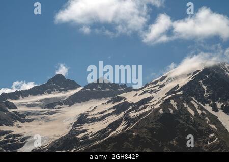 Snowy mountain slope with clouds on the background of a blue sky. The Caucasus mountains in summer. Glacier. Stock Photo