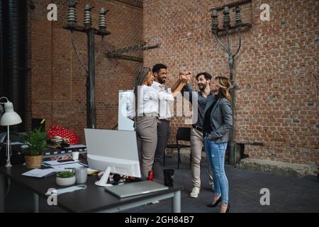 Cheerful young businesspeople standing in office, cooperation and celebrating new contract concept. Stock Photo