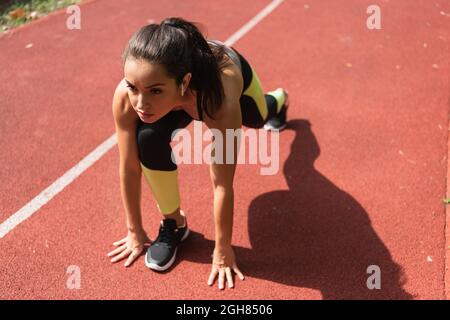 high angle view of sportswoman in wireless earphones standing in starting pose on stadium Stock Photo