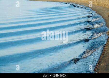 Small waves gently rolling in succession on the seashore at sunrise Stock Photo