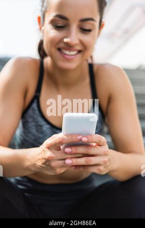 blurred and smiling sportswoman using smartphone outside Stock Photo