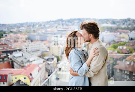 Happy young couple in love standing outdoors on balcony at home, kissing. Stock Photo