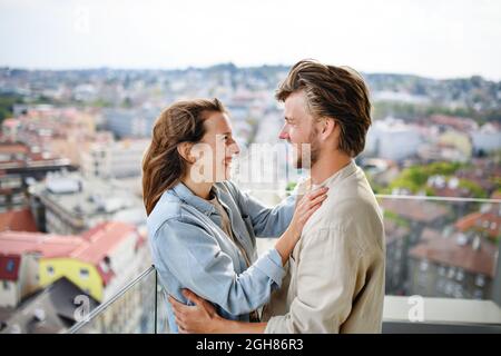 Happy young couple in love standing outdoors on balcony at home, looking at each other. Stock Photo