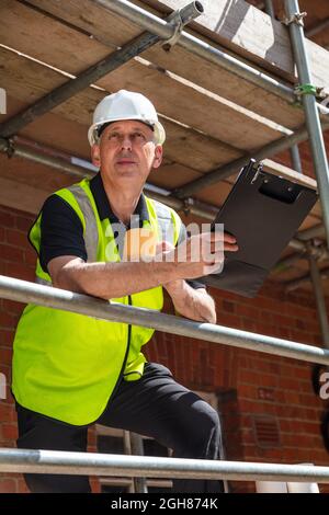 Male man builder foreman, construction worker or architect on site holding a clipboard and drinking a mug of coffee or tea Stock Photo