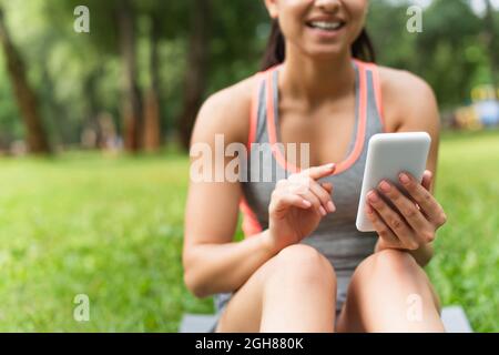 cropped view of cheerful and blurred sportswoman using smartphone in park Stock Photo