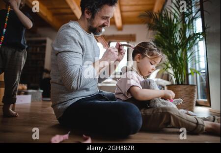 Mature father with small son and daugther resting indoors at home, playing and combing hair. Stock Photo