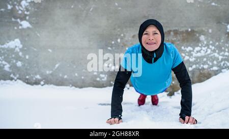 Active senior woman outdoors in snowy winter, doing push ups. Stock Photo