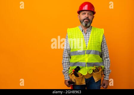 Middle-aged bearded man builder in uniform and hardhat with tools against orange background Stock Photo