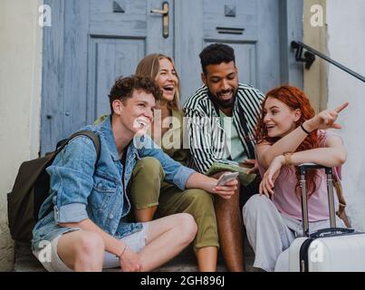 Group of young people outdoors on trip in town, resting and talking. Stock Photo