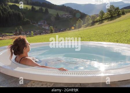 August 21, 2021: woman in a swimsuit from the back relaxes in an outdoor hot tub, with a green lawn Stock Photo