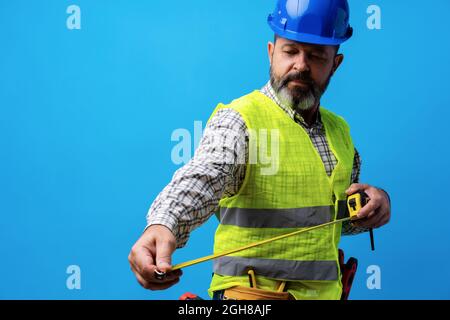 Male builder holding measuring roulette against blue background Stock Photo