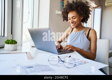High-spirited dark-haired woman typing on her laptop Stock Photo
