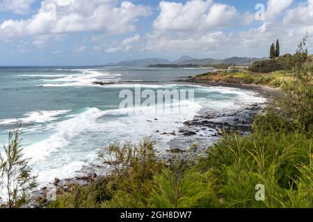 Ocean waves break on the volcanic rocks strewn along the shore in Kapaa, Kauai, Hawaii. Stock Photo