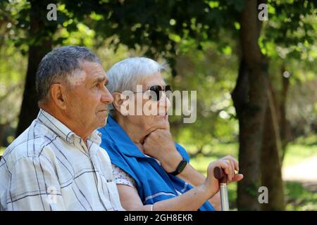 Elderly couple sitting with walking sticks on a bench. Leisure in park, life in retirement Stock Photo