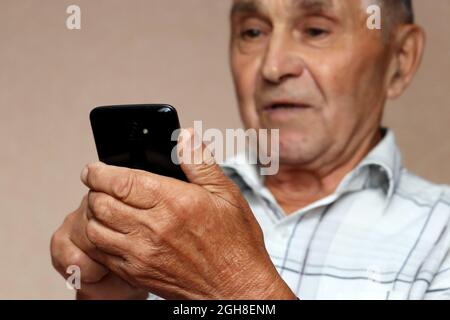 Elderly man using mobile phone, looking surprised on smartphone screen. Concept of online communication in retirement, winning, sms, reading news Stock Photo