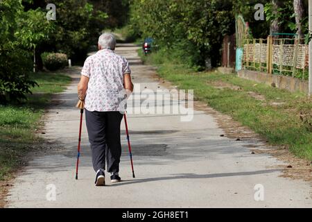 Old woman walking with a cane on a street. Limping person, diseases of the spine, life of elderly people Stock Photo