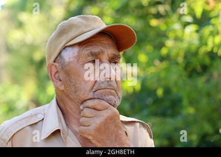 Portrait of pensive elderly man on green nature background. Concept of life in village, old age Stock Photo