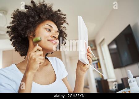Calm lady doing a facial massage with a jade roller Stock Photo