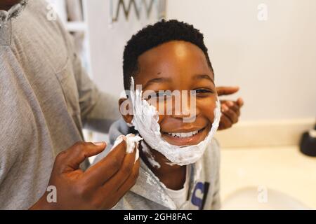 Portrait of african american son having fun with father and shaving foam in bathroom Stock Photo