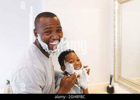 Portrait of smiling african american father with son having fun with shaving foam in bathroom Stock Photo